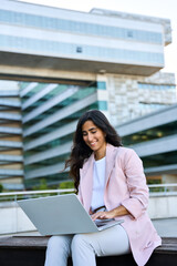 Wall Mural - Focused young middle eastern Israel businesswoman using laptop pc online application for work sitting outdoors. Indian or arabic woman manager in business suit working, typing on computer. Vertical