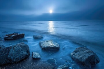Wall Mural - A beautiful blue ocean with a large moon reflecting on the water. The moon is positioned above the water, creating a serene and peaceful atmosphere