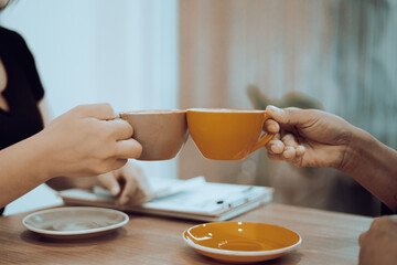 Close-up of a man and woman clinking coffee cups while talking at work.