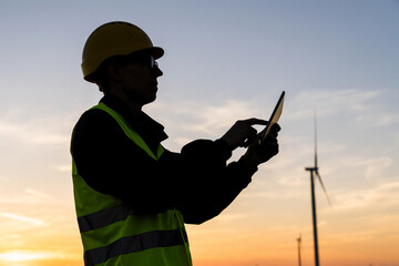 Canvas Print - Engineer with digital tablet works on a field of wind turbines at sunset