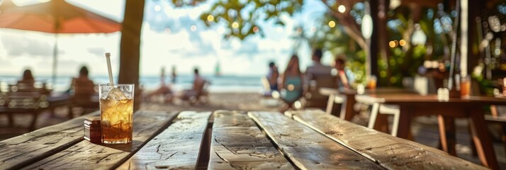 A glass of iced tea sits on a wooden table in a beachside cafe with a blurred background of other cafe patrons and the ocean