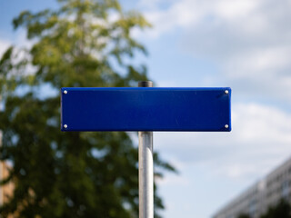 Empty street name sign as a template and copy space. Blue metal plate in front of a tree and the sky. Location guide showing the direction at a crossing in Germany.