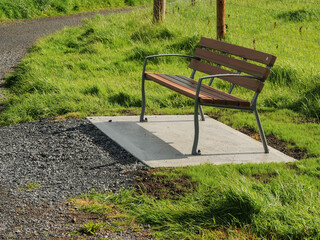 Wall Mural - A bench is sitting on a concrete slab in a grassy area of a park. The bench is empty and the grass is green. Warm sunny day. Metal and plastic materials