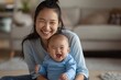 © Luiri Art - Asian mother with black hair in a ponytail, smiling while holding her laughing baby in a blue onesie, sitting on the floor in a bright living room in the morning light