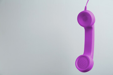 Wall Mural - Purple telephone handset hanging on light grey background. Space for text