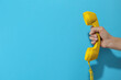 © New Africa - Woman holding yellow telephone handset on light blue background, closeup. Space for text