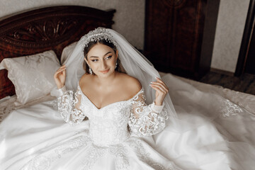 Wall Mural - A woman in a wedding dress is sitting on a bed. She is wearing a veil and a tiara