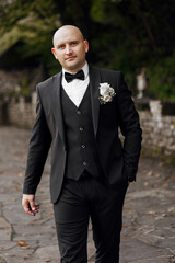 Wall Mural - A man in a black suit and white shirt is standing on a brick walkway. He is wearing a black tie and a black vest