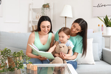 Young lesbian couple with adopted little girl reading book at home