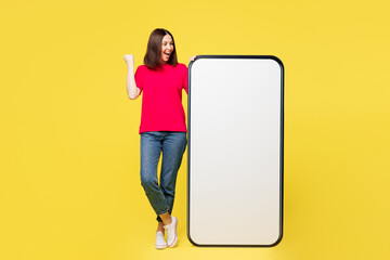 Full body young woman she wear pink t-shirt casual clothes big huge blank screen mobile cell phone smartphone with area do winner gesture isolated on plain yellow orange background. Lifestyle concept.