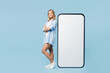 © ViDi Studio - Full body young happy woman wear white top shirt casual clothes stand near big huge blank screen mobile cell phone smartphone with area isolated on plain light blue cyan background. Lifestyle concept.