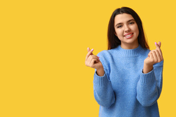 Wall Mural - Beautiful young girl showing heart gesture on yellow background. Valentine's Day celebration