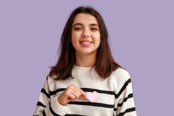 Wall Mural - Happy young girl with pink paper heart on purple background. Valentine's Day celebration