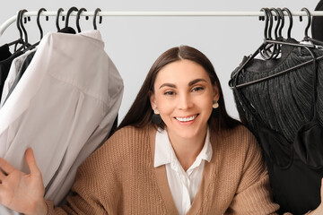 Sticker - Happy female stylist with clothes on rack against grey background