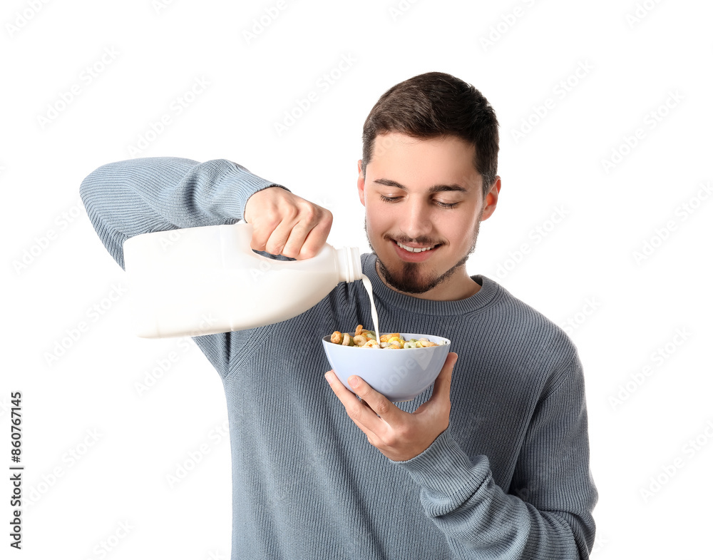 Handsome young man pouring milk into bowl with cereal rings on white background