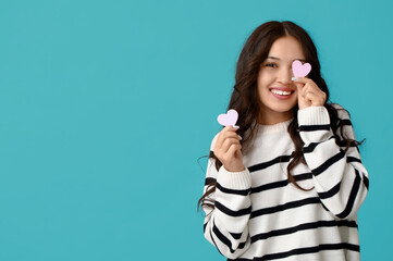 Wall Mural - Happy young Asian woman with pink paper hearts on blue background. Valentine's Day celebration