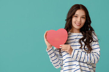 Wall Mural - Beautiful young Asian woman with red paper heart on blue background. Valentine's Day celebration