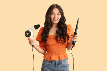 Sticker - Young Asian woman with curling iron and hair dryer on beige background