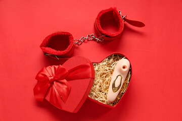 Wall Mural - Heart-shaped gift box with vibrator and handcuffs on red background. Valentine's Day celebration