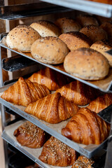 Close-up of freshly baked bread and croissants displayed on a rack in a bakery. Variety of baked goods