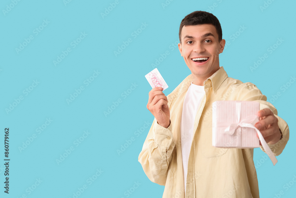 Handsome man with gift card and present on blue background