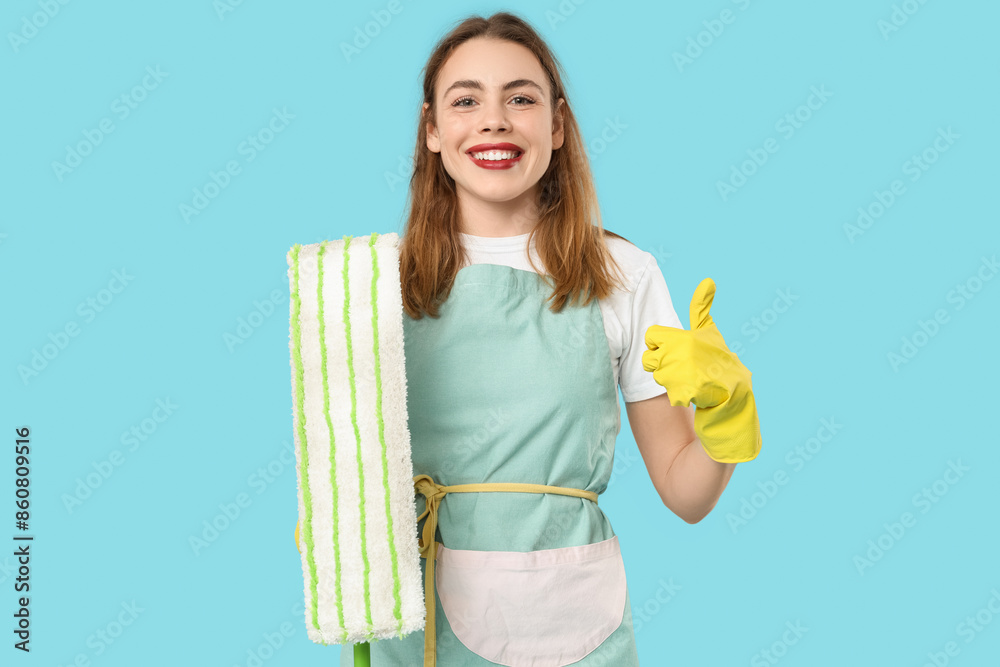 Pretty woman with mop showing thumb-up on blue background