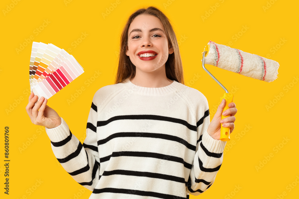 Young woman with color palettes and paint roller on yellow background