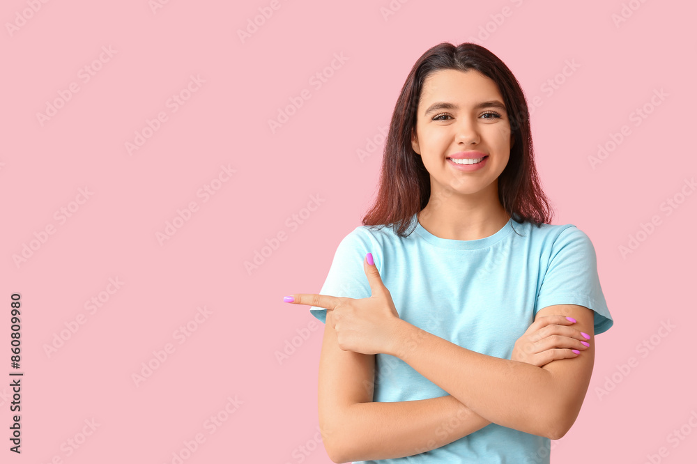 Young happy smiling woman pointing at something on pink background