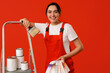 © Pixel-Shot - Female painter with color palettes, brush and cans of paint on stepladder against red background