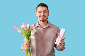 Wall Mural - Handsome man with gift box and tulips on blue background