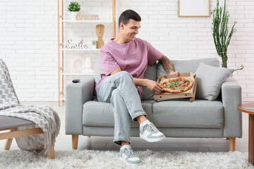 Wall Mural - Young man and cardboard box with tasty pizza on sofa at home