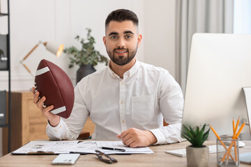 Wall Mural - Young man with american football ball at table in office