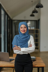 Wall Mural - Modern office Muslim businesswoman wearing a hijab stands smiling confidently working on a financial project. Do analysis, calculations, startup business ideas, e-commerce, online.