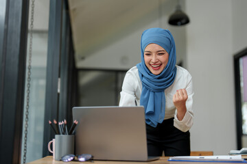 Wall Mural - Modern office Muslim businesswoman wearing hijab sits with laptop online, doing paperwork Sitting and working on financial projects, analysis, calculations, startup business ideas, e-commerce, online.