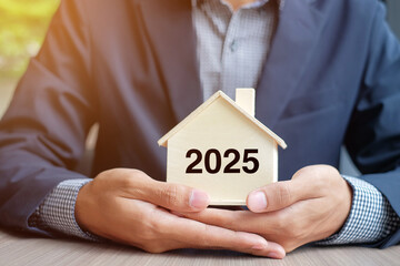 Sticker - Businessman hands holding wooden House model with 2025 New Year text. Property insurance and real estate concepts