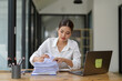 © Phimwilai - Asian businesswoman searches documents piled up on desk with laptop to do finance on office table, taxes, reports, accounting, online marketing, statistics, startup business concept.