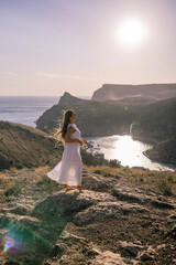 Wall Mural - woman stands on a rocky hill overlooking a body of water. She is wearing a white dress and she is enjoying the view.