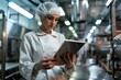 © Maxim Borbut - An attractive female worker in sterile clothes checks the production line using a tablet.