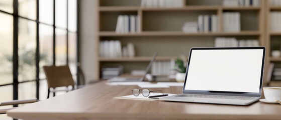 Wall Mural - a laptop computer with a white-screen mockup on a wood meeting table in a contemporary meeting room.