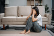 © laddawan - Asian woman sit Depression Dark haired  pensive glance Standing by window and anxiety Copy space with a blanket on a sofa.