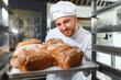 © Serhii - Male baker holding a tray of baked breads in bakery shop