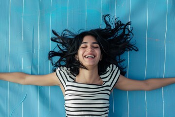 Canvas Print - Portrait of young woman with mid length black hair jumping for joy expressing her mood. Shot in studio on blue background with stripped pattern behind the model.