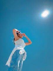 Vertical photo of happy asian Thai woman wear sun glasses standing under blue sky on sunny day, on vacation in summer.