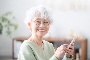 Wall Mural - smiling senior woman holding a smart phone (smartphone), looking at the camera tap or operate