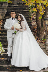 Wall Mural - A bride and groom are posing for a picture on a staircase. The bride is wearing a white dress and the groom is wearing a suit. The bride is holding a bouquet and the groom is holding a bouquet as well