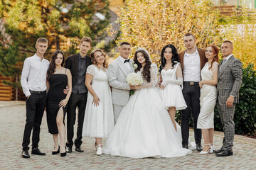 Wall Mural - A group of people are posing for a picture, including a bride and groom. The bride is wearing a white dress and the groom is wearing a suit. The group is standing in front of a building