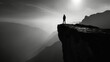 © Justlight - A man stands on the edge of a cliff his silhouette blending with the dark shadows of the mountains behind him. Black and white art