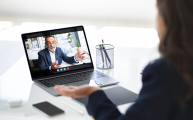 Poster - A businesswoman sits at her desk, engaged in a video call with a colleague on her laptop. She has a serious expression on her face, listening intently to the man on the screen