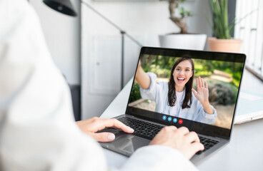 Poster - A woman is sitting at a desk in an office setting and video chatting with a person on her laptop. The person on the other end of the call is waving to the camera.