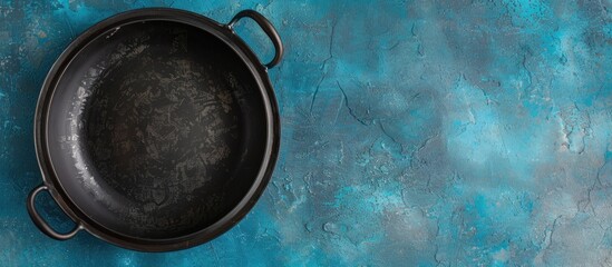 Poster - Bird's eye view of a vacant black ceramic bowl with two handles set against a blue concrete backdrop, providing ample copy space image.